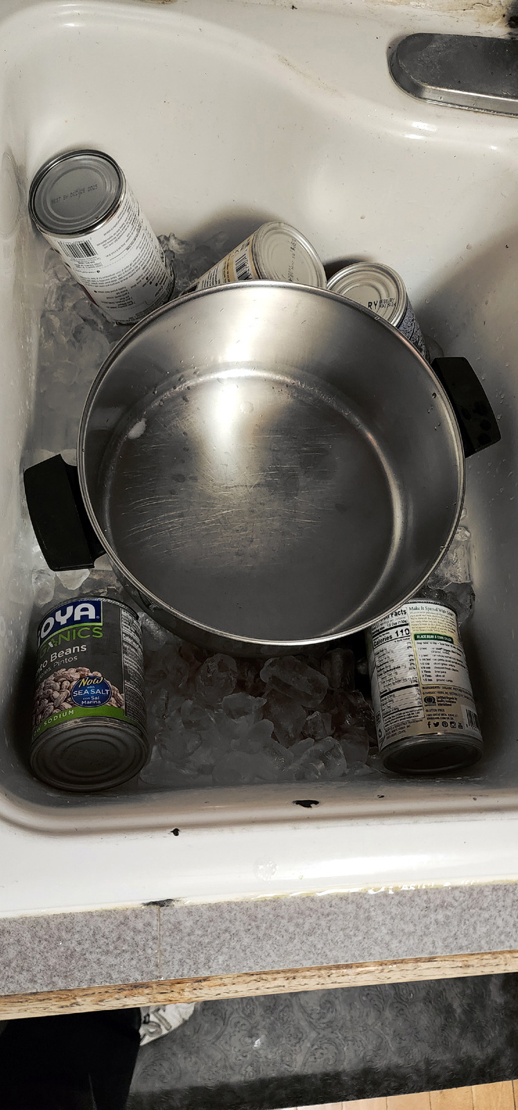 Cans of beans draining into ice at the bottom of a sink
